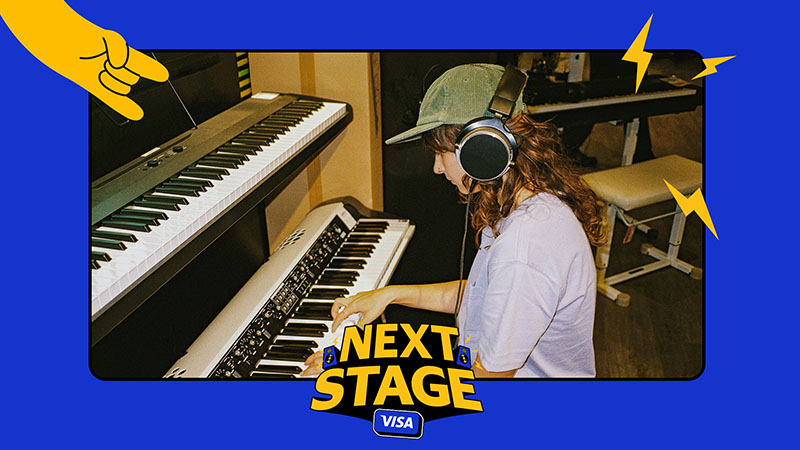 Person wearing headphones playing an electronic keyboard in a music studio, with Next Stage Visa branding.