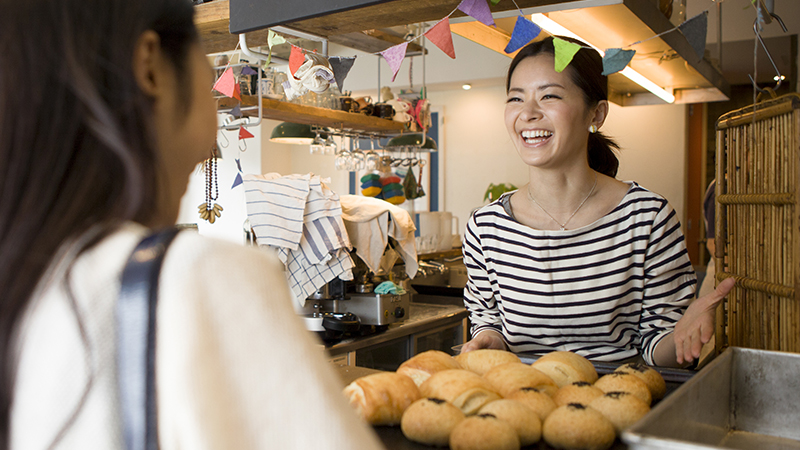 A smiling merchant bakery owner engaging with a customer.