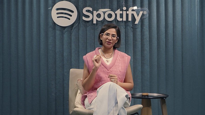 Woman seated in front of a Spotify logo, speaking in a studio setting