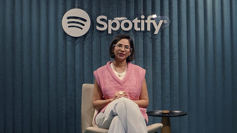 Woman sitting in a chair beneath a Spotify logo in a studio