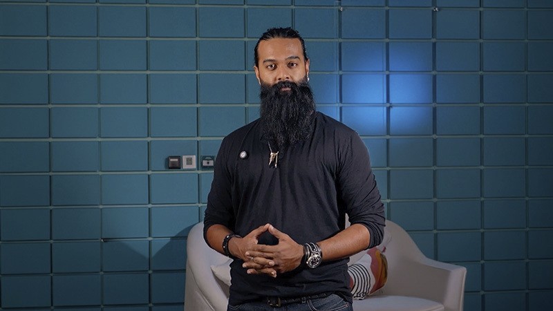 Bearded man standing indoors against a blue tiled wall