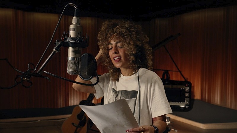 Woman singing in a recording studio while holding lyric sheets