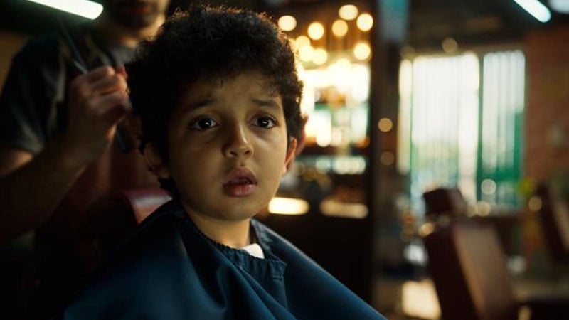 A boy in a barber's chair, a hairdresser standing behind him